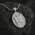 Load image into Gallery viewer, Polished silver Saint George pendant necklace on textured volcanic rock, centered macro jewelry photo with detailed dragon slayer relief and bright silver highlights.