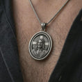 Load image into Gallery viewer, Oxidized spinning Jesus Christ pendant necklace worn on the chest, close-up lifestyle jewelry photo showing the Christian medallion on a spiga chain with dark clothing.