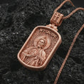 Load image into Gallery viewer, Rose gold plated Saint Jude dog tag pendant necklace on textured volcanic rock, detailed macro product shot with soft warm reflections and devotional Saint Jude design.