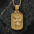 Load image into Gallery viewer, Gold plated Saint Dominic dog tag pendant necklace on textured volcanic rock, premium close-up studio composition emphasizing the saint figure, sacred book, and lily symbolism.
