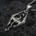 Load image into Gallery viewer, Oxidized Skyrim dragon pendant necklace on textured volcanic rock, close-up studio shot highlighting the angular dragon emblem, openwork design, and antique silver contrast.