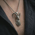 Load image into Gallery viewer, Oxidized ram horn pendant necklace worn on the chest, close-up lifestyle jewelry photo showing the Aries goat talisman on a spiga chain with dark clothing.