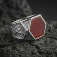 Load image into Gallery viewer, A red onyx signet ring in a polished silver finish resting on porous volcanic rock in a premium macro studio shot.