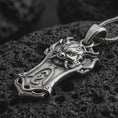 Load image into Gallery viewer, An oxidized Taurus bull pendant rests on dark volcanic rock in a macro studio close-up, showing a horned animal head over a shield-inspired frame.