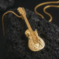 Load image into Gallery viewer, Gold plated skull guitar pendant necklace on textured volcanic rock, premium close-up studio composition emphasizing the electric guitar shape, skull motif, and rock and roll symbolism.