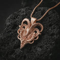 Load image into Gallery viewer, Rose gold plated biomechanical ram skull pendant necklace on textured volcanic rock, detailed macro product shot with soft warm reflections and dark fantasy animal symbolism.