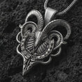 Load image into Gallery viewer, Oxidized biomechanical ram skull pendant necklace on textured volcanic rock, close-up studio shot highlighting the curved horns, skeletal ram face, cyber gothic details, and antique silver contrast.