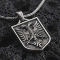 Load image into Gallery viewer, Oxidized double-headed eagle shield pendant necklace on textured volcanic rock, close-up studio shot highlighting the twin eagle heads, spread wings, crest frame, and antique silver contrast.