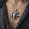 Load image into Gallery viewer, Polished silver ram skull pendant necklace worn on the chest, masculine lifestyle shot highlighting the sculpted skull, curled horns, and bright silver finish.