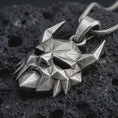 Load image into Gallery viewer, An oxidized Surtur pendant rests on dark volcanic rock in a macro studio close-up, showing a sharp horned mask with angular Norse fantasy detail.