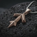 Load image into Gallery viewer, A Bronze Tyr rune pendant rests on dark volcanic rock in a macro studio close-up, showing the Teiwaz symbol in a bold geometric Norse design.