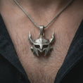 Load image into Gallery viewer, An oxidized Helm of Awe inspired mask pendant is worn on the neck in a close-up lifestyle shot, centered on the chest as a powerful Norse amulet.