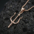 Load image into Gallery viewer, Rose gold plated Poseidon trident pendant necklace on textured volcanic rock, detailed macro product shot with soft warm reflections and ancient sea god symbolism.