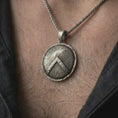 Load image into Gallery viewer, Oxidized Spartan shield pendant necklace worn on the chest, close-up lifestyle jewelry photo showing the ancient warrior medallion on a spiga chain with dark clothing.