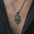 Load image into Gallery viewer, Oxidized hamsa hand pendant necklace worn on the chest, close-up lifestyle jewelry photo showing the protective evil eye amulet on a spiga chain with dark clothing.