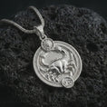 Load image into Gallery viewer, Polished silver Cancer zodiac pendant necklace on textured volcanic rock, centered macro jewelry photo with detailed crab horoscope relief and bright silver highlights.