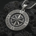 Load image into Gallery viewer, Oxidized Greek compass pendant necklace on textured volcanic rock, close-up studio shot highlighting the raised compass rose, north south letters, Greek key border, and antique silver contrast.