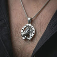 Load image into Gallery viewer, Polished silver horseshoe pendant necklace worn on the chest, masculine lifestyle shot highlighting the bright silver finish, horseshoe shape, and sculpted horse relief.