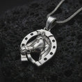 Load image into Gallery viewer, Polished silver horseshoe pendant necklace on textured volcanic rock, centered macro jewelry photo with detailed horse profile, bridle accents, and bright silver highlights.
