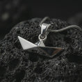 Load image into Gallery viewer, Polished silver origami boat pendant necklace on textured volcanic rock, centered macro jewelry photo with clean folded lines, angular silhouette, and bright silver highlights.