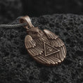 Load image into Gallery viewer, Bronze owl all-seeing eye pendant necklace on textured volcanic rock, close-up studio shot highlighting the winged owl relief, triangle eye symbol, feather details, and antique silver contrast.