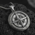 Load image into Gallery viewer, Oxidized compass pendant necklace on textured volcanic rock, close-up studio shot highlighting the raised compass rose, directional letters, ridged outer border, and antique silver contrast.