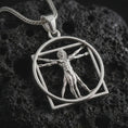 Load image into Gallery viewer, Polished silver Vitruvian Man pendant necklace on textured volcanic rock, centered macro jewelry photo with detailed anatomical figure relief and bright silver highlights.
