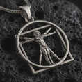 Load image into Gallery viewer, Oxidized Vitruvian Man pendant necklace on textured volcanic rock, close-up studio shot highlighting the Leonardo da Vinci figure, circular frame, geometric square outline, and antique silver contrast.