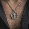 Load image into Gallery viewer, Polished silver Vitruvian Man pendant necklace worn on the chest, masculine lifestyle shot highlighting the bright silver finish, sculpted figure, and geometric frame.