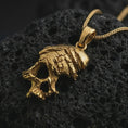 Load image into Gallery viewer, Gold plated cracked skull pendant necklace on textured volcanic rock, premium close-up studio composition emphasizing the edgy skull silhouette, jagged cracks, and dark punk jewelry design.