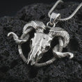 Load image into Gallery viewer, Polished silver ram skull pendant necklace on textured volcanic rock, centered macro jewelry photo with detailed horn engraving, skull texture, and bright silver highlights.
