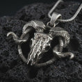 Load image into Gallery viewer, Oxidized ram skull pendant necklace on textured volcanic rock, close-up studio shot highlighting the cracked skull, curled horns, skeletal details, and antique silver contrast.
