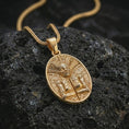 Load image into Gallery viewer, A gold plated Aztec mask pendant lies on textured volcanic rock in a dramatic studio macro shot, highlighting the ancient tribal amulet design.