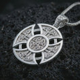 Load image into Gallery viewer, Polished silver Celtic cross pendant necklace on textured volcanic rock, centered macro jewelry photo with detailed knotwork engraving and bright silver highlights.