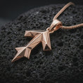 Load image into Gallery viewer, A rose gold plated Tyr rune pendant is photographed on porous volcanic rock in a close-up studio composition with refined luxury lighting and faceted sculptural detail.