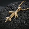 Load image into Gallery viewer, A gold plated Tyr rune pendant lies on textured volcanic rock in a dramatic studio macro shot, highlighting the Teiwaz symbol and Viking-inspired form.