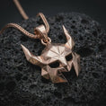 Load image into Gallery viewer, A rose gold plated Helm of Awe inspired mask pendant is photographed on porous volcanic rock in a close-up studio composition with bold luxury lighting.