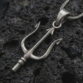 Load image into Gallery viewer, Oxidized Poseidon trident pendant necklace on textured volcanic rock, close-up studio shot highlighting the three-prong spear, sharp tips, mythological form, and antique silver contrast.