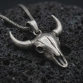 Load image into Gallery viewer, Oxidized bull skull pendant necklace on textured volcanic rock, close-up studio shot highlighting the long horns, hollow skull form, western design, and antique silver contrast.