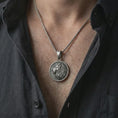 Load image into Gallery viewer, Oxidized Lion of Judah pendant necklace worn on the chest, close-up lifestyle jewelry photo showing the lion medallion on a spiga chain with dark clothing.