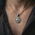 Load image into Gallery viewer, Oxidized lotus flower pendant necklace worn on the chest, close-up lifestyle jewelry photo showing the spiritual lotus medallion on a spiga chain with dark clothing.