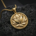 Load image into Gallery viewer, Gold plated lotus flower pendant necklace on textured volcanic rock, premium close-up studio composition emphasizing the blooming lotus design, circular frame, and spiritual yoga symbolism.