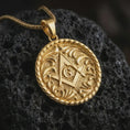 Load image into Gallery viewer, Gold plated Masonic pendant necklace on textured volcanic rock, premium close-up studio composition emphasizing the square, compass, G symbol, and decorative medallion border.