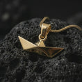 Load image into Gallery viewer, Gold plated origami boat pendant necklace on textured volcanic rock, premium close-up studio composition emphasizing the minimalist paper boat design, sharp geometry, and symbolic journey charm.