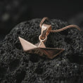 Load image into Gallery viewer, Rose gold plated origami boat pendant necklace on textured volcanic rock, detailed macro product shot with soft warm reflections and elegant folded boat styling.