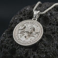 Load image into Gallery viewer, Polished silver Baphomet pendant necklace on textured volcanic rock, centered macro jewelry photo with detailed ram horns, symbolic lettering, and bright silver highlights.