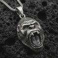 Load image into Gallery viewer, An oxidized gorilla pendant rests on dark volcanic rock in a macro studio close-up, showing a fierce roaring ape head with detailed teeth and fur texture.