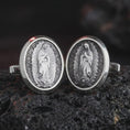 Load image into Gallery viewer, An oxidized Our Lady of Guadalupe cufflink pair rests on dark volcanic rock in a macro studio close-up, showing the Virgin Mary relief in oval frames.