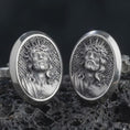 Load image into Gallery viewer, An oxidized Jesus Crown of Thorns cufflink pair rests on dark volcanic rock in a macro studio close-up, showing a detailed Christ portrait inside oval frames.