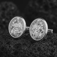 Load image into Gallery viewer, Polished silver Saint Joseph cufflinks resting on textured volcanic rock in a premium macro composition, highlighting the detailed religious relief and oval medallion design.